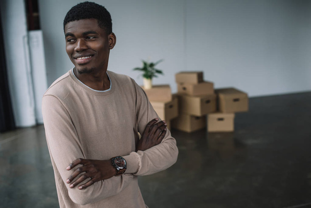 smiling african american man standing with crossed arms and looking away in new office during relocation - Foto, immagini