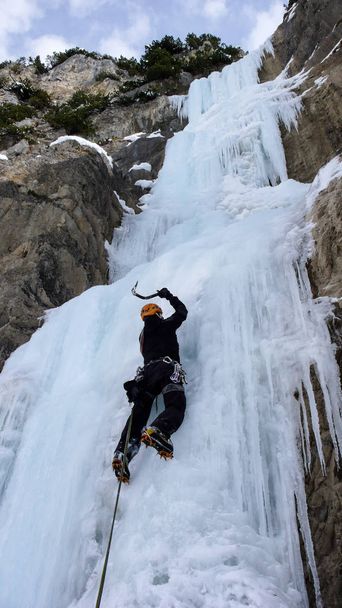 male ice climber on a steep frozen waterfall on a beautiful winter day in the Swiss Alps - Photo, Image