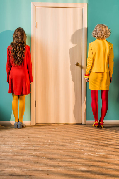 vista trasera de las mujeres de estilo retro de pie en la puerta en el apartamento colorido, concepto de casa de muñecas
 - Foto, Imagen