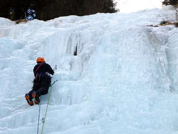 male mountain guide lead ice climbing a frozen waterfall in deep winter in the Alps of Switzerland - Photo, Image