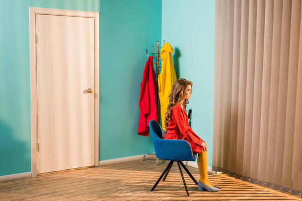 side view of pensive retro styled woman sitting on chair at bright apartment, doll house concept - Photo, Image
