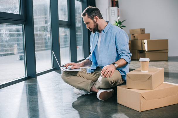 homem de negócios barbudo usando laptop enquanto sentado no chão no novo escritório
 - Foto, Imagem
