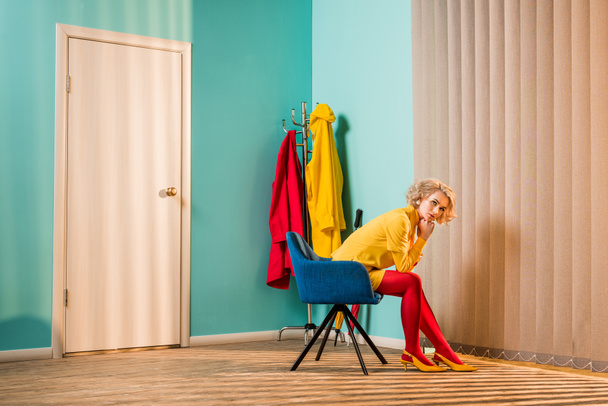 side view of retro styled woman sitting on chair at bright apartment, doll house concept - Фото, зображення