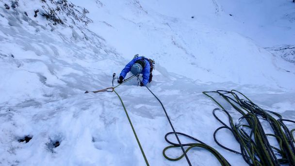 hombre escalador de hielo en una chaqueta azul en una empinada cascada congelada en invierno profundo en los Alpes de Suiza
 - Foto, Imagen