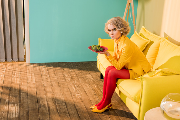 mujer de estilo retro con brócoli en la placa descansando en el sofá en el apartamento luminoso, concepto de casa de muñecas
 - Foto, Imagen
