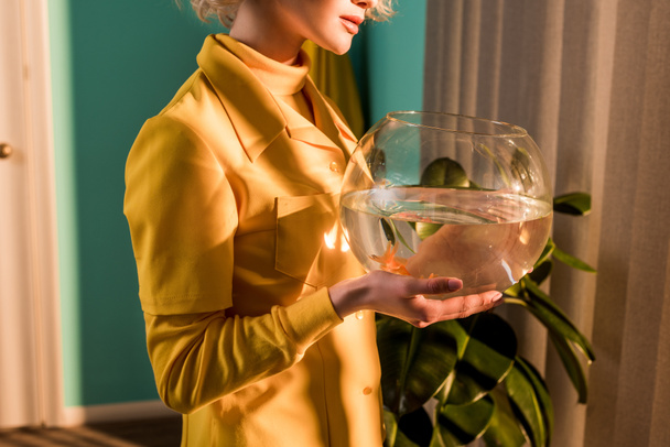 cropped image of stylish woman holding aquarium with gold fish at home - Foto, Bild