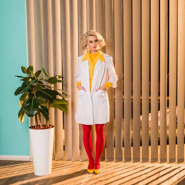 beautiful retro styled doctor standing in white coat and red tights in clinic - Foto, afbeelding