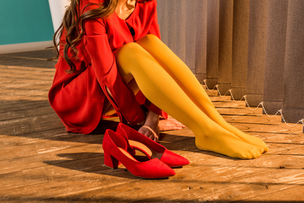 обрезанное изображение женщины в красном платье в стиле ретро, сидящей на полу возле жалюзи дома
 - Фото, изображение