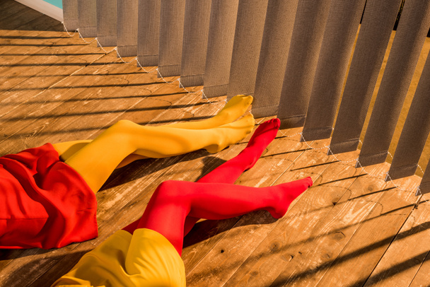 обрезанный образ девочек в красочных колготках и платьях, лежащих на полу возле жалюзи
 - Фото, изображение