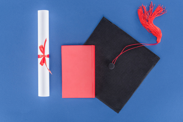 Tapa de graduación con diploma y libro aislado en azul
 - Foto, Imagen