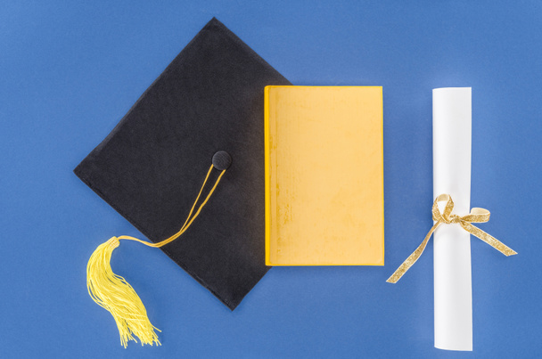Sombrero de graduación con diploma y libro aislado en azul
 - Foto, imagen