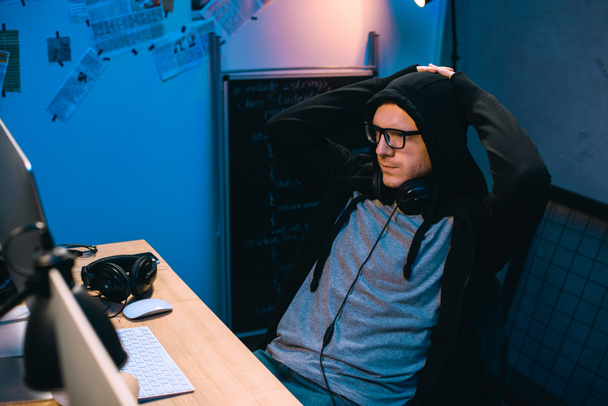 hacker encapuchado relajarse en la silla delante de su lugar de trabajo
 - Foto, imagen