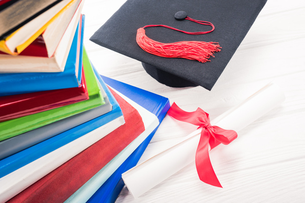 Ballagási kalap és a diploma, a fehér asztal mellett halmozott könyvek - Fotó, kép