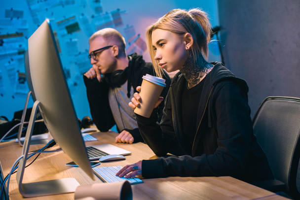 młodych kobiet hakera, picia kawy i pracę na złośliwe oprogramowanie z wspólnikiem - Zdjęcie, obraz