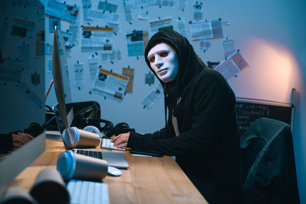 хакер в масці, що розробляє шкідливі програми на своєму робочому місці
 - Фото, зображення