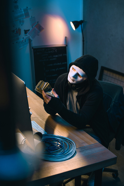 hacker in mask counting stolen money at his workplace - Foto, Imagem