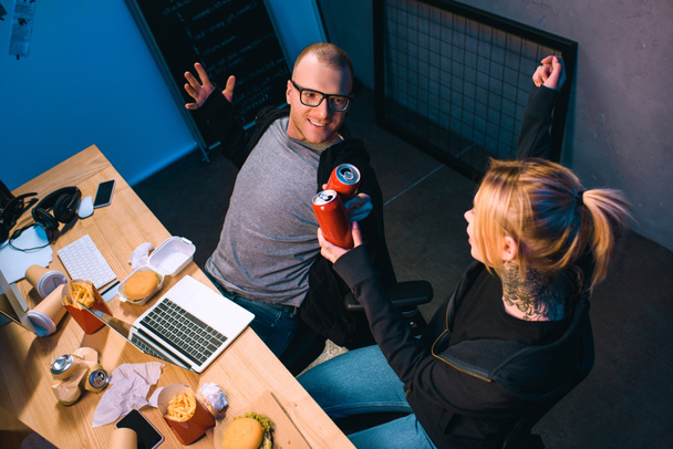 vista ad alto angolo di celebrare coppia di hacker clinking lattine di birra sul posto di lavoro
 - Foto, immagini