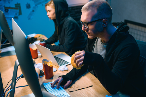 hacker masculino que trabaja en malware con cómplice y comer comida chatarra
 - Foto, imagen