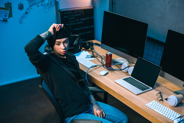 joven hacker mujer en frente de escritorio quitándose la máscara
 - Foto, imagen