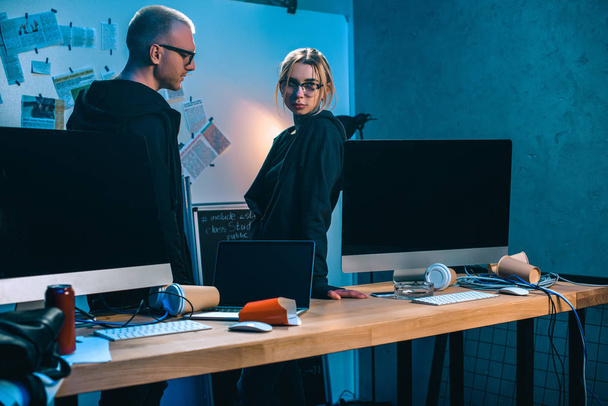 coppia di hacker in piedi vicino alla scrivania con computer in camera oscura
 - Foto, immagini
