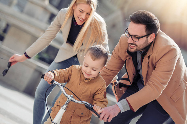 young family with son on bicycle walking in city  - Photo, Image