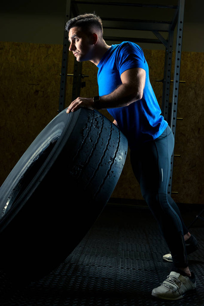 strong young athlete with a large heavy wheel in the gym - Fotó, kép