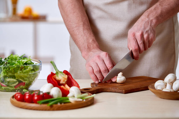 Man cooking at kitchen making healthy vegetable salad, close-up, selective focus. - Photo, Image