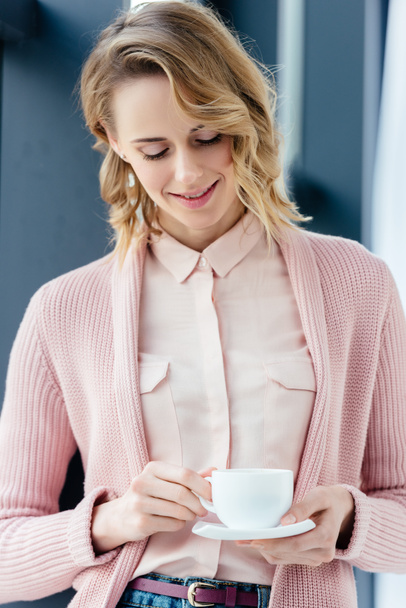 portrait of smiling woman looking at cup of coffee in hands - Fotó, kép