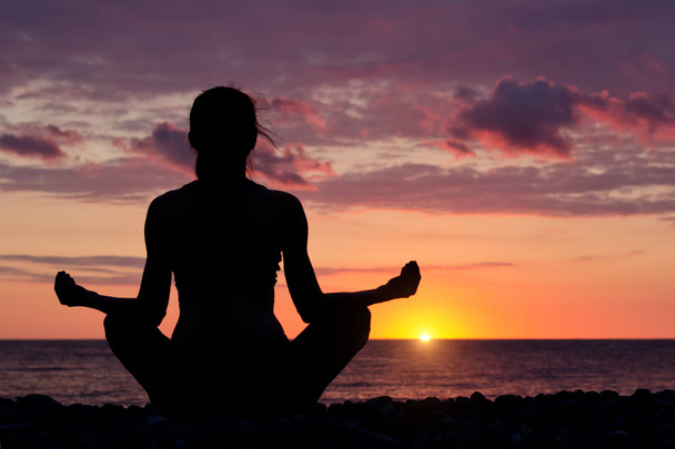 Woman meditating on the beach in lotus position. Silhouette, sunset - Foto, Imagen