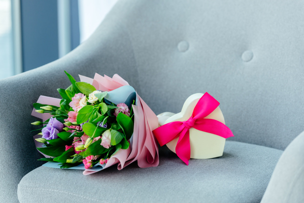 close up view of wrapped bouquet of flowers and heart shaped gift box with ribbon on armchair, mothers day concept - Fotografie, Obrázek