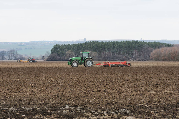 zwei Traktoren pflügen ein Feld im Wald unter blauem Himmel mit Wolken - Tschechische Republik - Foto, Bild