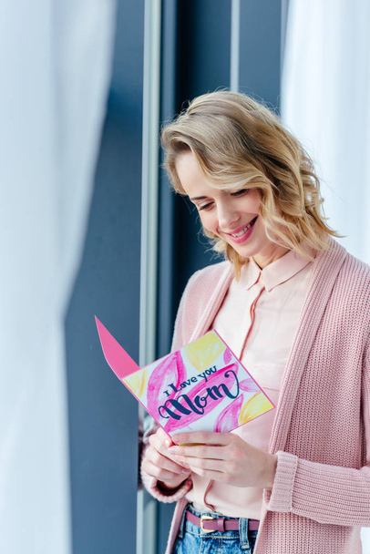 smiling woman reading i love you mom postcard in hands, mothers day holiday concept - Photo, Image