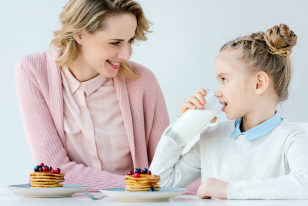 happy mother and daughter having breakfast together at table - 写真・画像