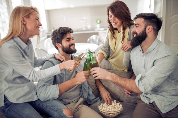 Allegro gruppo di amici che bevono birra e mangiano popcorn a casa
 - Foto, immagini