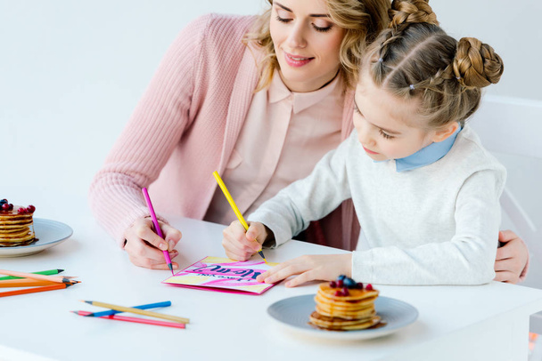 portrait of mother and daughter making greeting postcard together at table - Foto, afbeelding
