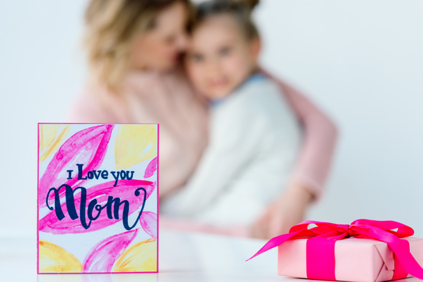 selective focus of i love you mom postcard, wrapped gift and hugging family on background - Photo, Image