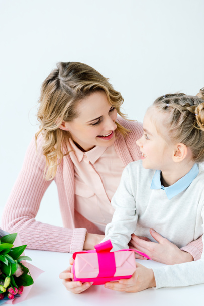 portrait of smiling mother hugging little cute daughter with wrapped gift in hands, mothers day holiday concept - Photo, Image