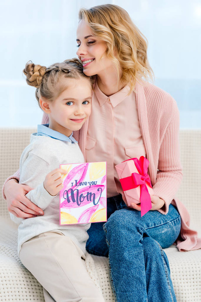 mother hugging adorable daughter and showing postcard on happy mothers day - Photo, Image