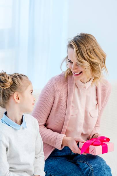 smiling mother holding gift box and looking at daughter on happy mothers day - Zdjęcie, obraz