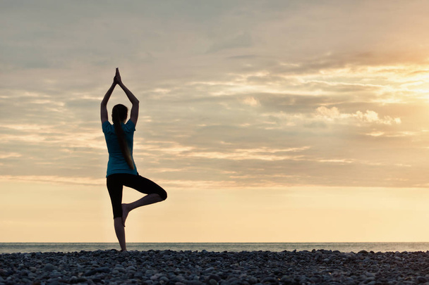 Girl at sunset practicing yoga at the seashore, back view - Foto, immagini
