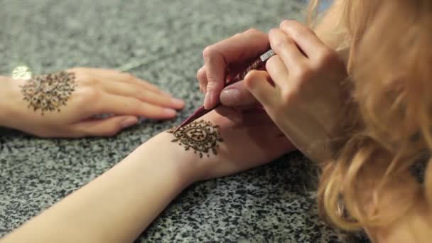 Mujer haciendo mehendi floral en una mano con henna en una mesa
. - Metraje, vídeo