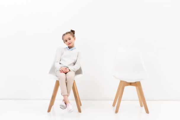 adorable child sitting on chair and looking at camera on white - Photo, Image