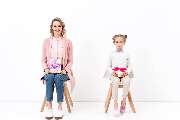 mother and daughter sitting on chairs with postcard and bouquet, happy mothers day concept - 写真・画像