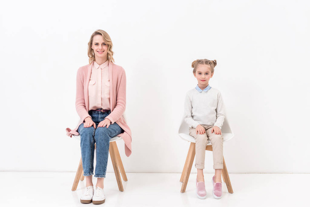 anya és lánya székeken ülnek, és látszó-nél fényképezőgép fehér - Fotó, kép