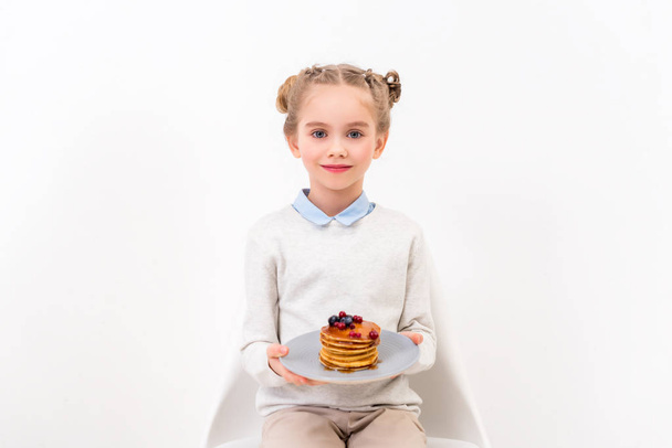 adorable child holding plate with pancakes and looking at camera isolated on white - Photo, Image