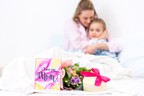 mother and daughter lying on bed with presents on foreground, happy mothers day concept - 写真・画像