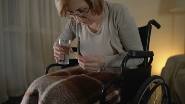 Old woman in wheelchair taking pill with shaking hands, sad life in nursing home - Materiał filmowy, wideo