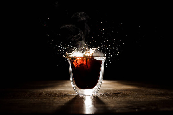 Splash of the hot coffee from the transparent glass on the dark background - Photo, Image