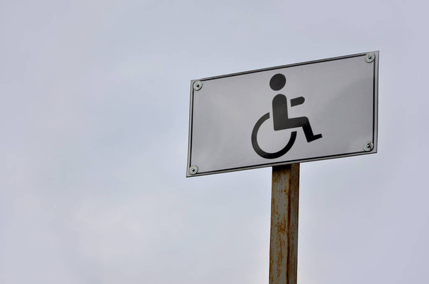 Un cartello stradale che indica l'incrocio di una strada per disabili. Insegna stradale bianca con una foto di un uomo seduto su una sedia a rotelle
 - Foto, immagini
