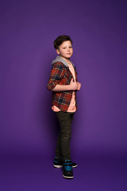 La joie de s'habiller est un art ! Pleine longueur vue de côté portrait de joyeux petit garçon debout sur fond violet isolé
. - Photo, image